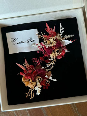 Two floral arrangements of red, brown, and white dried flowers rest on black fabric in a box with a "Camellia" card. This ensemble is as elegantly curated as the Customized Holiday Flower Ring by CAMELLIA. Two floral arrangements of red, brown, and white dried flowers rest on black fabric in a box with a "Camellia" card. This ensemble is as elegantly curated as the Customized Holiday Flower Ring by CAMELLIA.