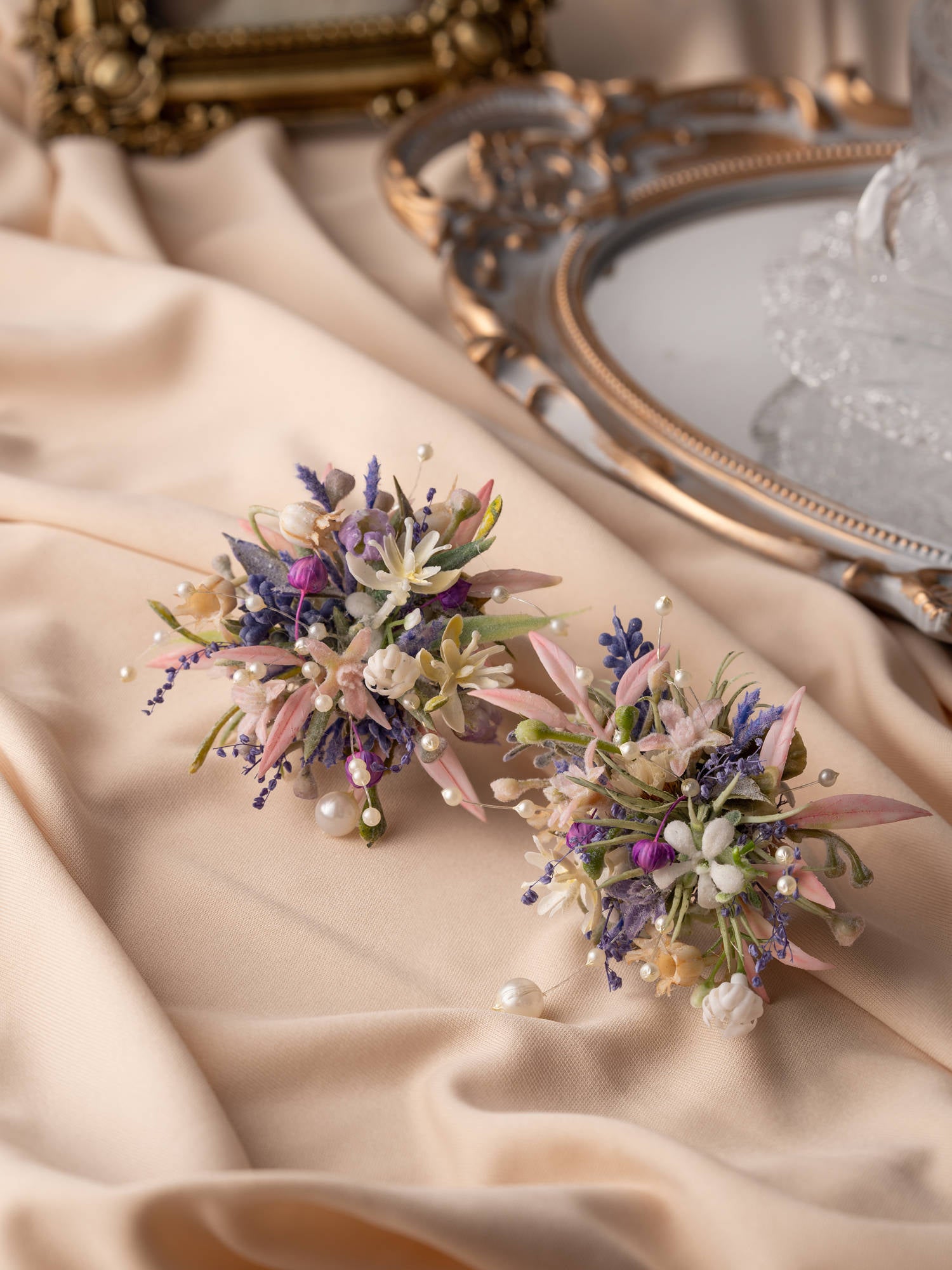 Two charming floral arrangements of Korean Purple Wedding Flower Rings by CAMELLIA sit on a beige fabric with ornate mirrors in the background. These displays are perfect for any occasion, echoing timeless beauty and adding elegance to any space.