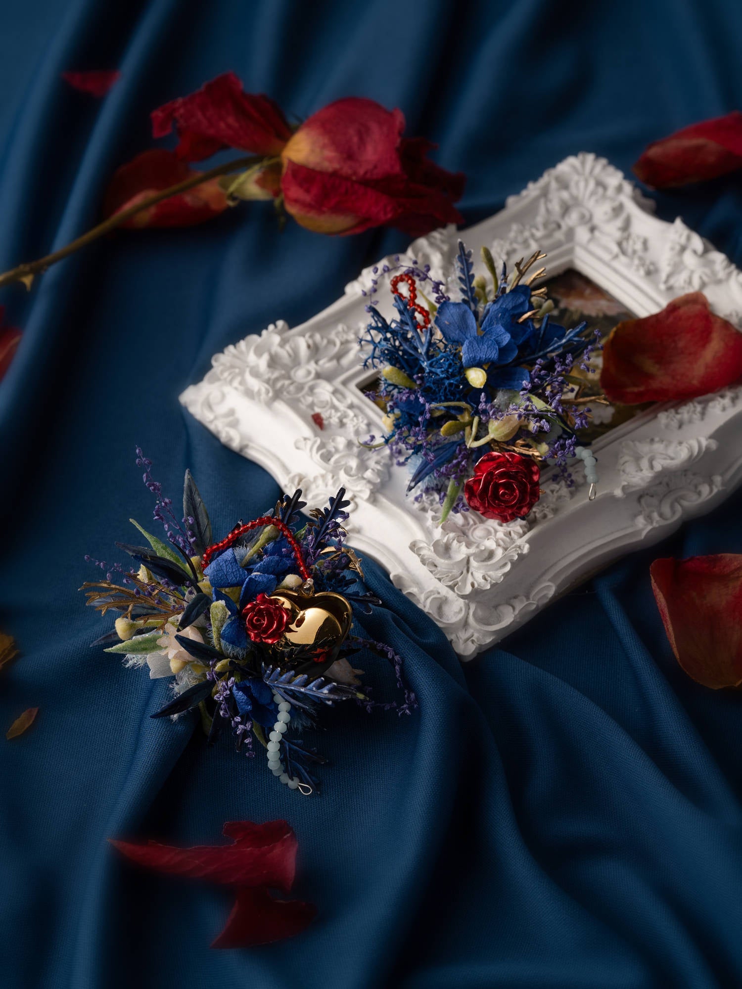 The "Little Prince Wedding Flower Rings" by CAMELLIA feature a red and blue floral arrangement on a white frame, set against blue fabric with preserved red petals. Handcrafted in New York, this piece brings elegance to any setting.