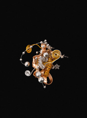 The Star Flower Ring by CAMELLIA resembles a complex abstract sculpture with intertwined metallic coils, spheres, and ribbons in gold and silver hues, evoking handcrafted jewelry artistry against a black background. The Star Flower Ring by CAMELLIA resembles a complex abstract sculpture with intertwined metallic coils, spheres, and ribbons in gold and silver hues, evoking handcrafted jewelry artistry against a black background.