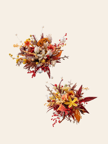 The two handcrafted burgundy Theater Style Wedding Flower Rings by CAMELLIA showcase a decorative arrangement of dried and artificial flowers in red, yellow, orange, and white hues on a light background. The two handcrafted burgundy Theater Style Wedding Flower Rings by CAMELLIA showcase a decorative arrangement of dried and artificial flowers in red, yellow, orange, and white hues on a light background.