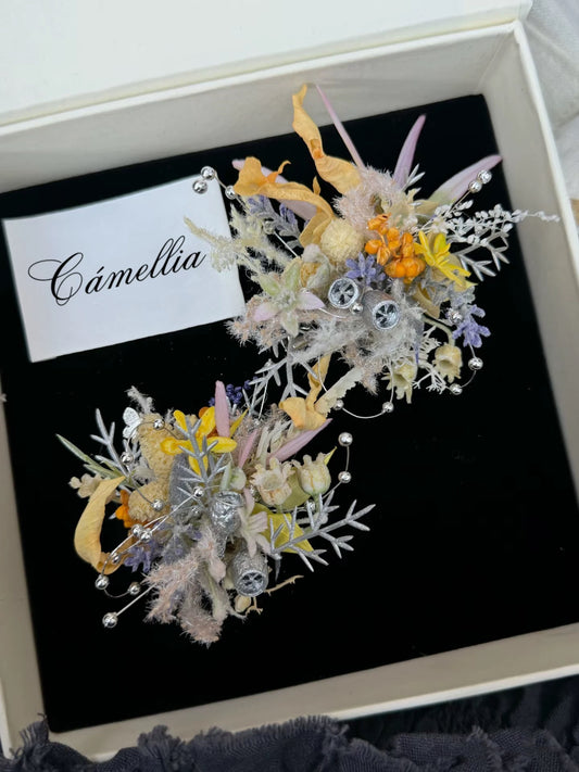 A variety of dried flowers with silver ornaments accompanies a card labeled