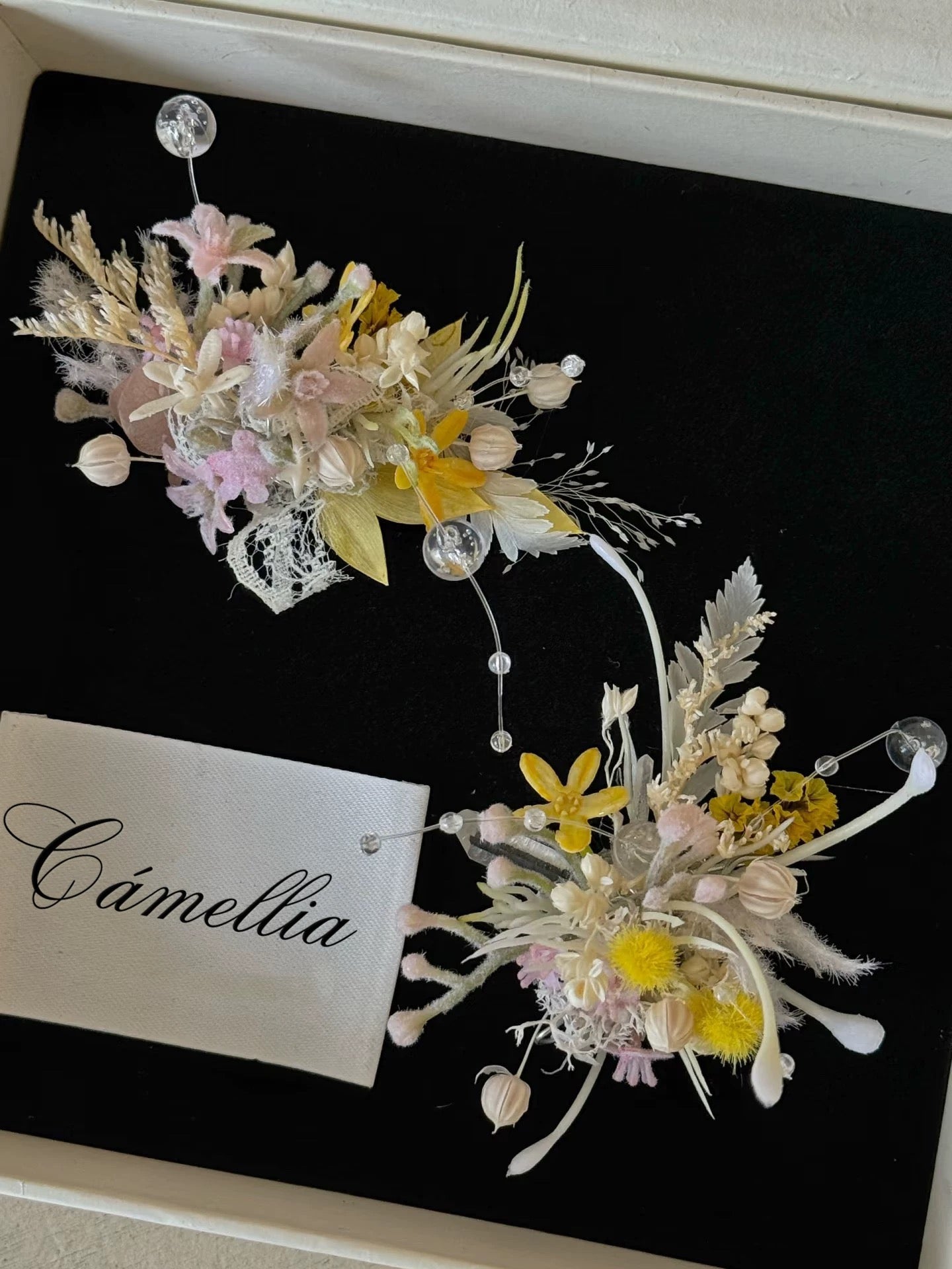 Elegant floral arrangements with pastel flowers and foliage on a black background, featuring customizable elements like a fabric label displaying "CAMELLIA," adorn the Customized Unique Flower Ring.