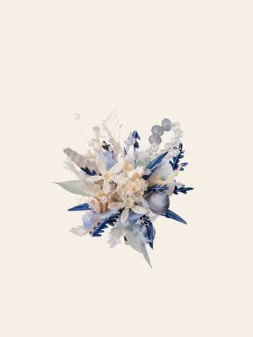 A decorative arrangement of blue and beige elements, with dried flowers, seashells, and foliage on a light background, evokes the handcrafted Ocean Flower Ring by CAMELLIA from New York. A decorative arrangement of blue and beige elements, with dried flowers, seashells, and foliage on a light background, evokes the handcrafted Ocean Flower Ring by CAMELLIA from New York.