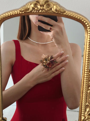 In a mirror selfie, a woman in a red dress wears a shimmering pearl necklace and holds small dried flowers. Her face is partly obscured by her phone, while the light catches her adjustable ring—a Customized Wedding Flower Ring by CAMELLIA—adding elegance to this intimate moment. In a mirror selfie, a woman in a red dress wears a shimmering pearl necklace and holds small dried flowers. Her face is partly obscured by her phone, while the light catches her adjustable ring—a Customized Wedding Flower Ring by CAMELLIA—adding elegance to this intimate moment.