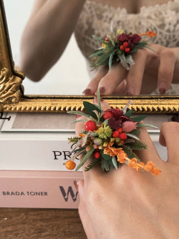 Reflected in a mirror, a person wears the CAMELLIA Customized Basic Flower Ring, handcrafted in New York. The adjustable ring has red, orange, and pink flowers with green leaves. Nearby, two books titled "Prada" and "Brada Toner" are visible. Reflected in a mirror, a person wears the CAMELLIA Customized Basic Flower Ring, handcrafted in New York. The adjustable ring has red, orange, and pink flowers with green leaves. Nearby, two books titled "Prada" and "Brada Toner" are visible.