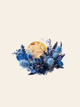 The Camellia Birth Flower Ring by CAMELLIA features a yellow rose amidst blue and purple foliage, including thistles and leaves, showcasing the exquisite art of handcrafted jewelry against a light background.