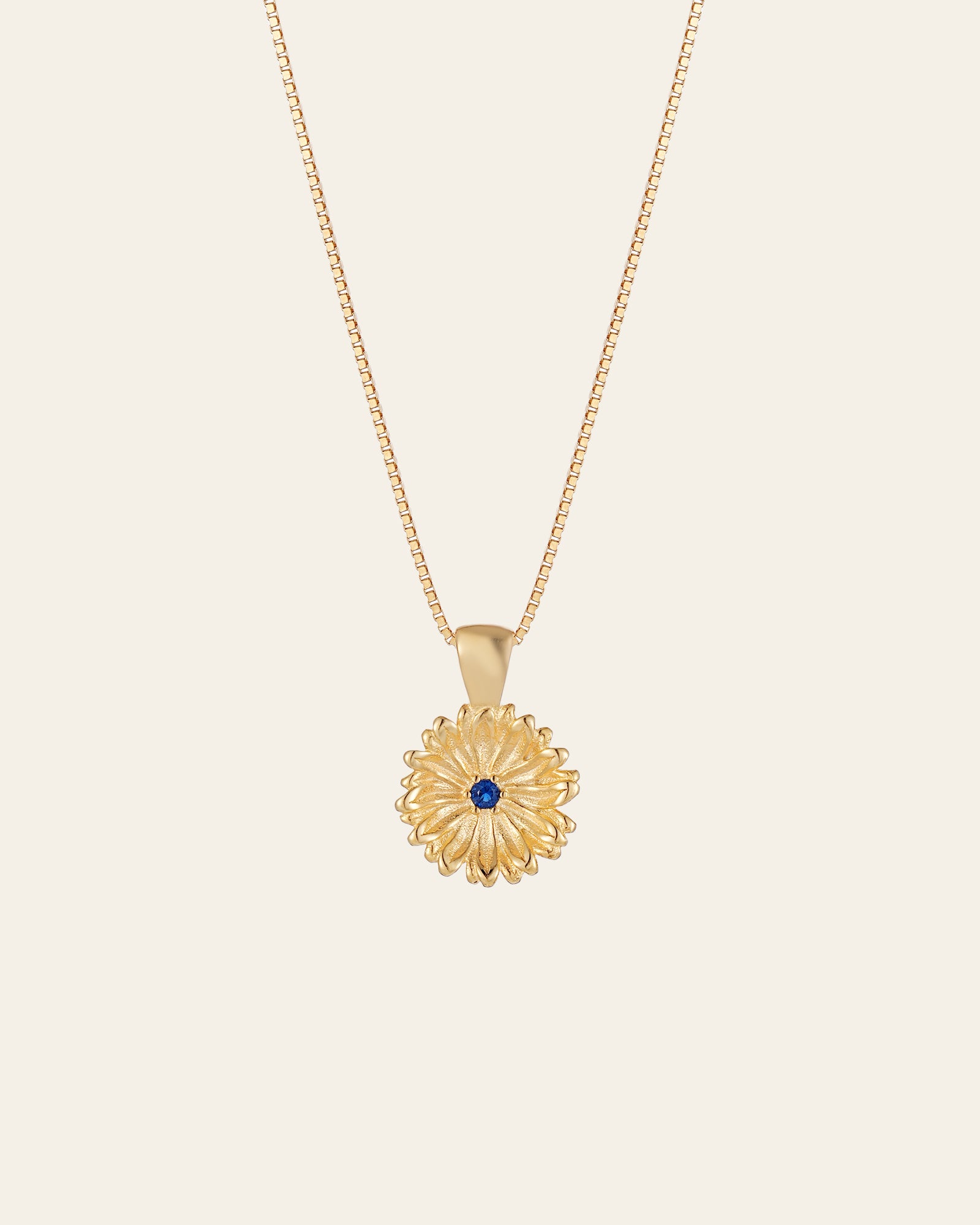 The Elsa Peony Sapphire Necklace by CAMELLIA features a sunflower-shaped pendant with a central blue gemstone, set in 14K yellow gold vermeil. Designed to be hypoallergenic, it's ideal for those with sensitive skin.