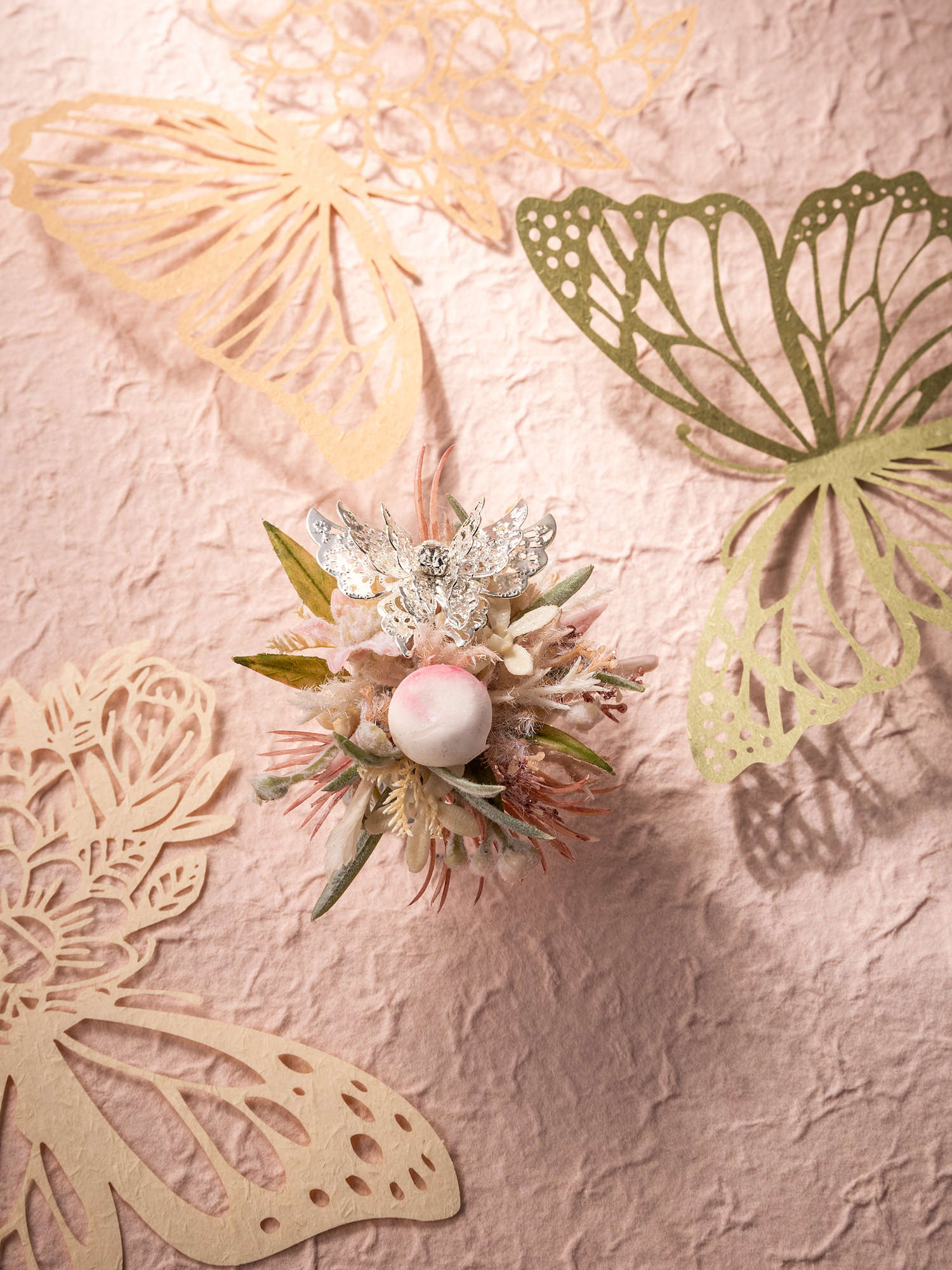 Handcrafted in New York, the CAMELLIA Butterfly Flower Ring showcases dried preserved flowers with a pearl ornament on pink textured paper, highlighted by beige and green cut-out butterflies.