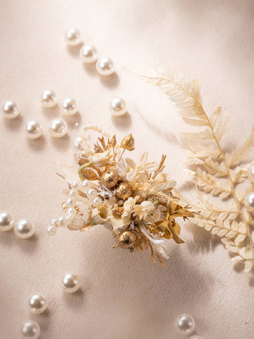 The Pearl Flower Ring by CAMELLIA features a beige textured surface with scattered pearls, dried flowers, and an artfully placed handcrafted fern leaf for a delicate and elegant display. The Pearl Flower Ring by CAMELLIA features a beige textured surface with scattered pearls, dried flowers, and an artfully placed handcrafted fern leaf for a delicate and elegant display.