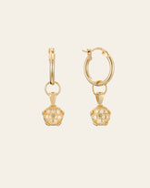 The Elsa Poppy Peridot Earrings by CAMELLIA, crafted in hypoallergenic 14K Yellow Gold Vermeil, feature gold hoops with flower-shaped pendants and are showcased against a cream background.