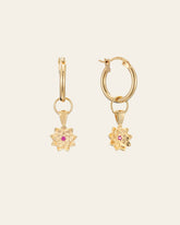 The Elsa Lotus Ruby Earrings by CAMELLIA are gold hoops with lotus-shaped pendants featuring small pink stones. Made from 14K yellow gold vermeil, these hypoallergenic earrings offer elegance and comfort for daily wear.