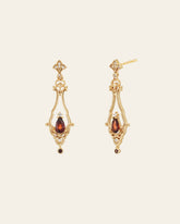 The Sophina Garnet Earrings by CAMELLIA feature gold ornate diamond-shaped tops with garnet teardrop gemstones, crafted in 14K Yellow Gold Vermeil against a plain background.