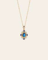 The CAMELLIA Eta Sapphire Necklace is a gold vermeil piece featuring an oval blue sapphire gemstone, elegantly surrounded by smaller blue and clear stones in a decorative pendant.