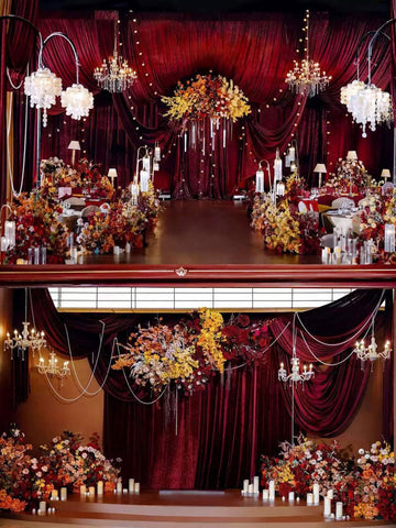 A lavish indoor setting features red drapery, chandeliers, abundant floral arrangements, candles, and a CAMELLIA burgundy Theater Style Wedding Flower Ring masterpiece to create an elegant event atmosphere. A lavish indoor setting features red drapery, chandeliers, abundant floral arrangements, candles, and a CAMELLIA burgundy Theater Style Wedding Flower Ring masterpiece to create an elegant event atmosphere.