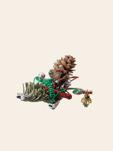 The CAMELLIA Christmas Flower Ring features pinecones, red and green metallic coils, silver spheres, and a gold dangler, set against a beige background.