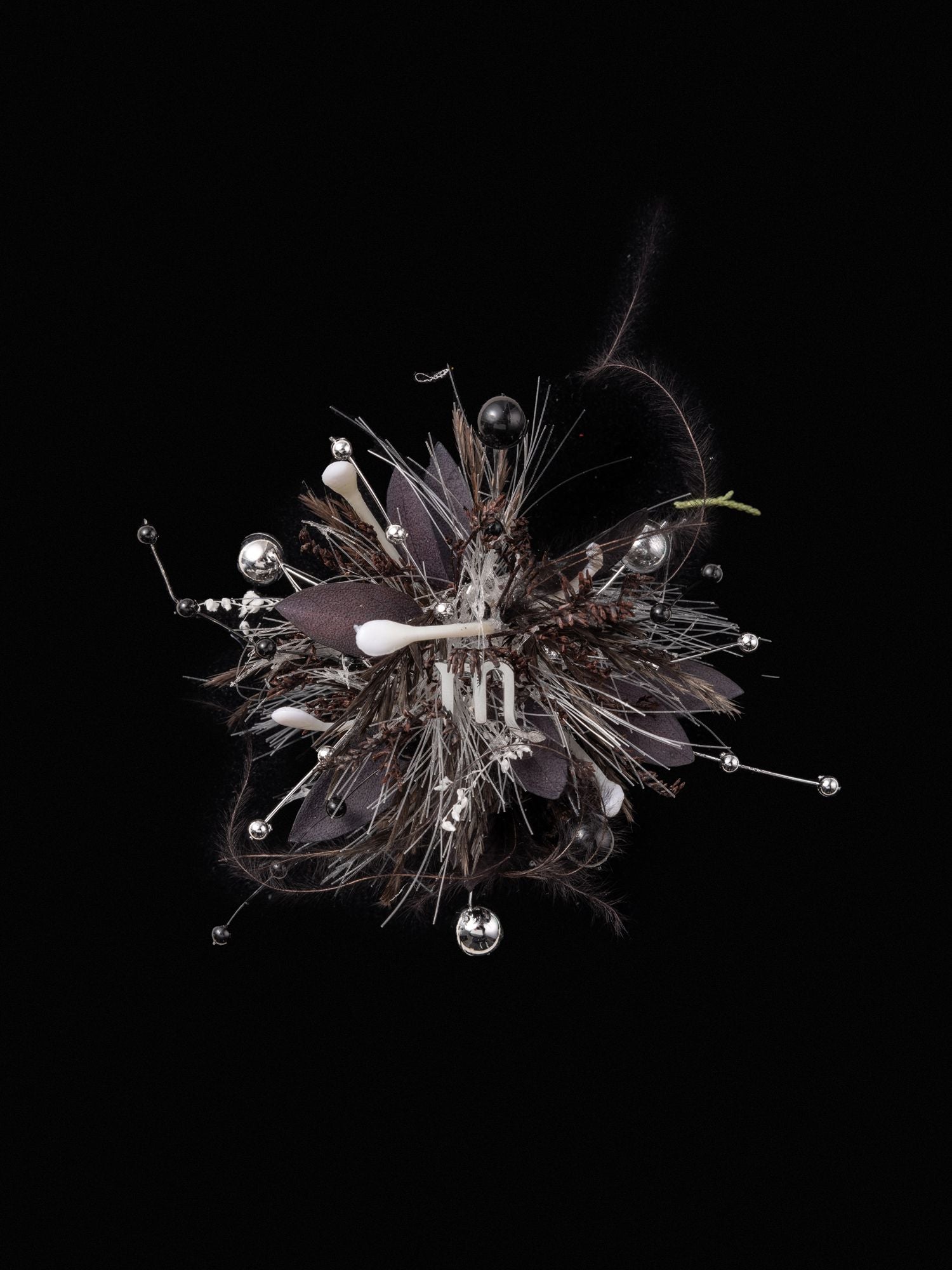 A complex handcrafted abstract sculpture resembling a cluster, featuring metallic pins, dark leaves, feathers, and a white central element against a black background. The piece evokes the intricate elegance of CAMELLIA's Scorpio Flower Ring or an adjustable custom symbol flower ring.