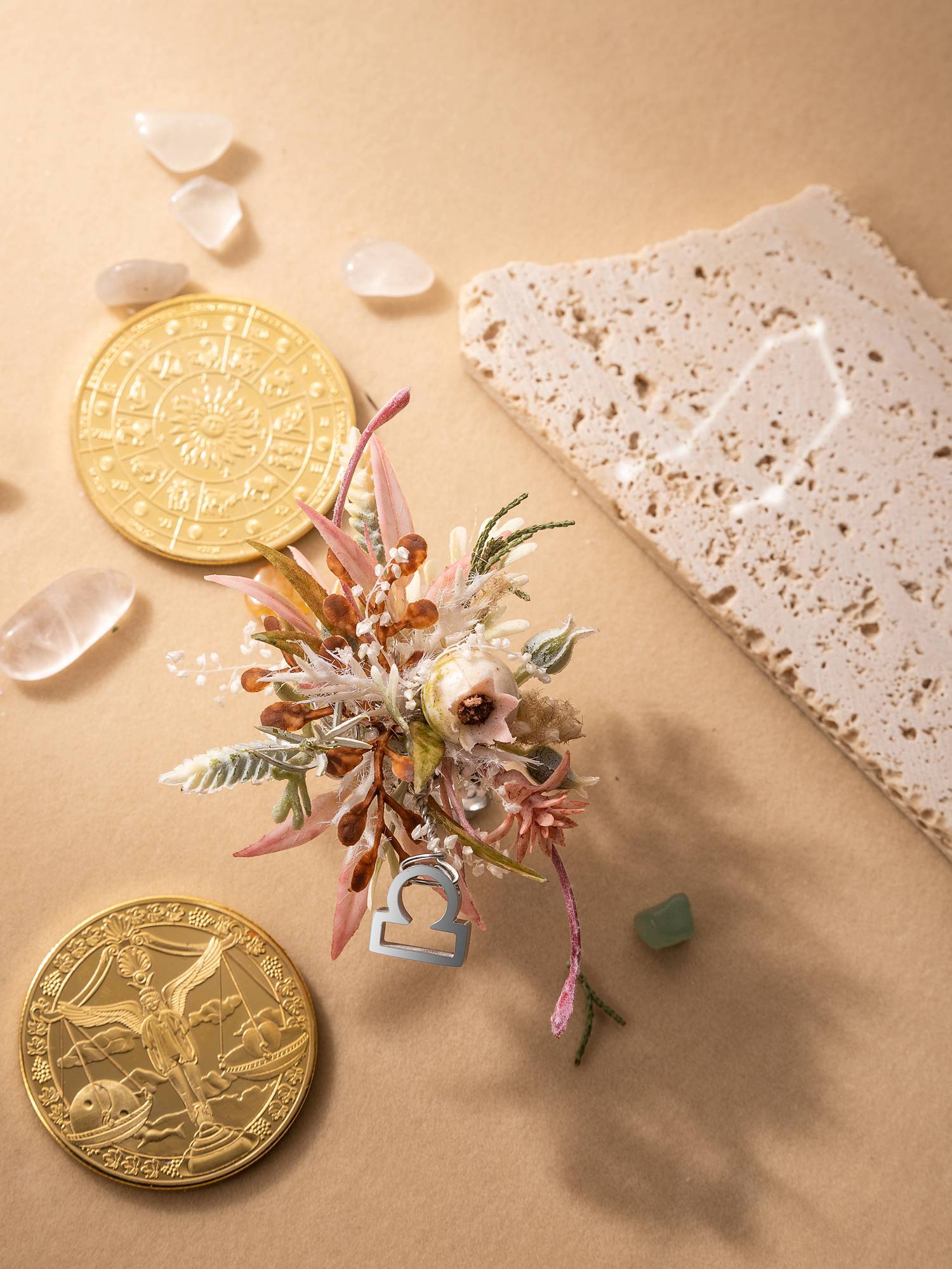 An arrangement features dried flowers, a Libra symbol, gold coins, clear stones, and textured paper on beige, accompanied by the adjustable handcrafted CAMELLIA Libra Flower Ring.