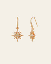The Stella Radiance Opal Dangle Earrings by CAMELLIA are exquisite yellow gold earrings with a sunburst design, accented by small gemstones and opal centers against a plain backdrop.