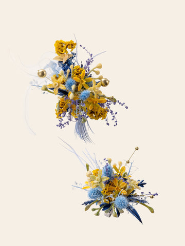 CAMELLIA's Van Gogh's Starry Wedding Flower Rings showcase clusters of blue and yellow artificial flowers and foliage with elements like small berries, thistles, and textured leaves against a plain beige background. CAMELLIA's Van Gogh's Starry Wedding Flower Rings showcase clusters of blue and yellow artificial flowers and foliage with elements like small berries, thistles, and textured leaves against a plain beige background.