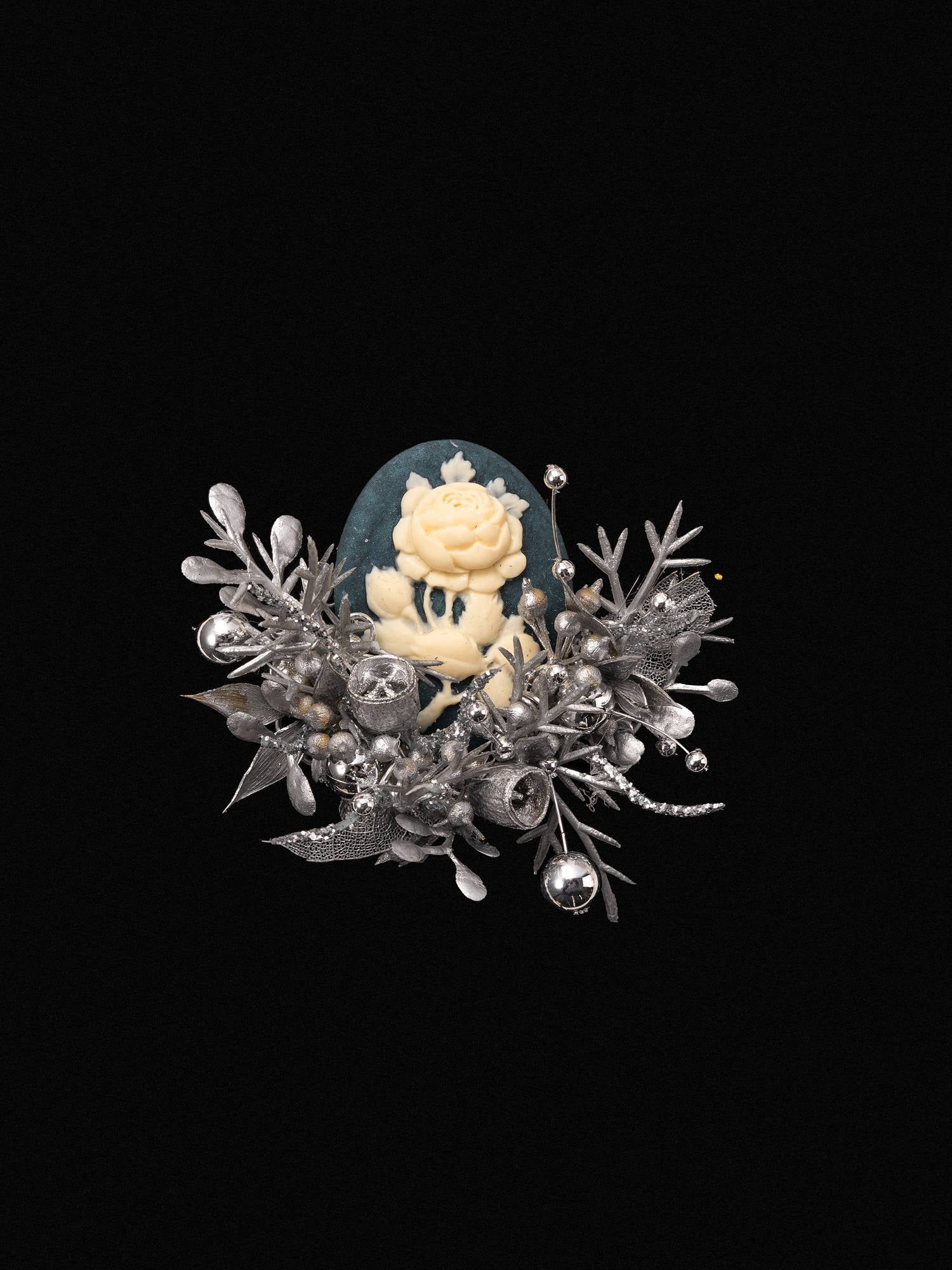 A handcrafted silver brooch features an intricate white rose on a blue backdrop, accented with delicate silver leaves and small round details over a black background, echoing the elegance of CAMELLIA's Cotton Rose Hibiscus Birth Flower Ring.