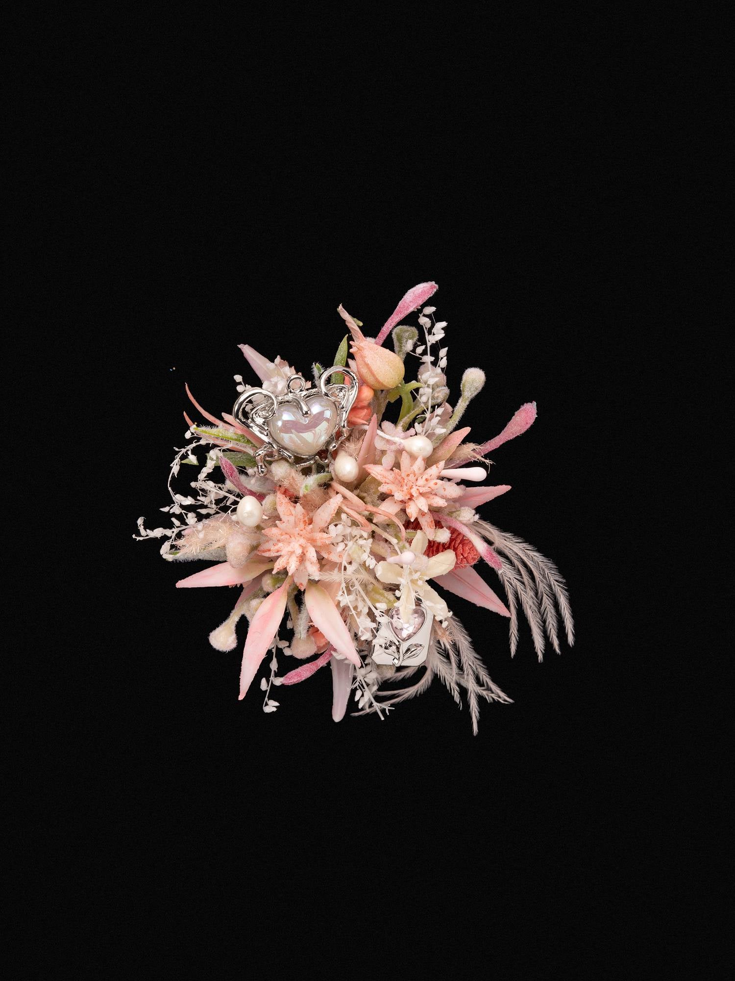 The Confession Valentine’s Day Flower Ring by CAMELLIA features a handcrafted bouquet of mixed pink and white dried preserved flowers with feathers and decorative elements against a black background, created in New York.