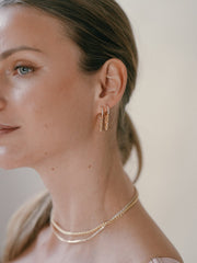 A woman with brown hair wearing CAMELLIA's Willo Cz Chain Hoop Earrings in 14K Yellow Gold Vermeil and a matching necklace exudes elegance.