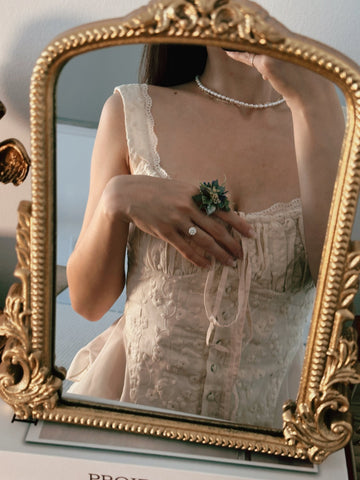 A person takes a mirror selfie wearing a white lace corset and pearl necklace, with hands adorned with the CAMELLIA Customized Basic Flower Ring. The ornate gold frame highlights the dress's intricate details, complemented by customizable jewelry handcrafted in New York. A person takes a mirror selfie wearing a white lace corset and pearl necklace, with hands adorned with the CAMELLIA Customized Basic Flower Ring. The ornate gold frame highlights the dress's intricate details, complemented by customizable jewelry handcrafted in New York.