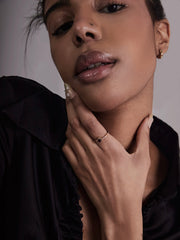 A person in a black top and vintage-inspired gold jewelry poses, showcasing the CAMELLIA 14K Solid Gold Carena Garnet Ring on polished nails, with natural makeup and their hand gently touching their neck.