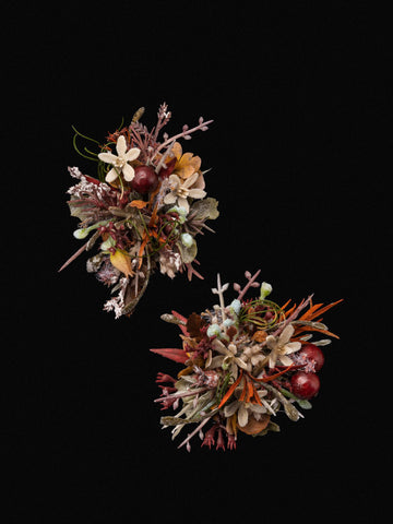 Two handcrafted Medieval Gothic Wedding Flower Rings by CAMELLIA, featuring various dried flowers and greenery, are positioned diagonally on a black background. Two handcrafted Medieval Gothic Wedding Flower Rings by CAMELLIA, featuring various dried flowers and greenery, are positioned diagonally on a black background.