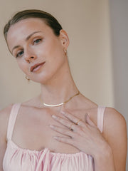 Dressed in a pink top, a person elegantly poses with one hand on their chest adorned with CAMELLIA's exquisite 25mm Mother Hoops in 14K Yellow Gold Vermeil.