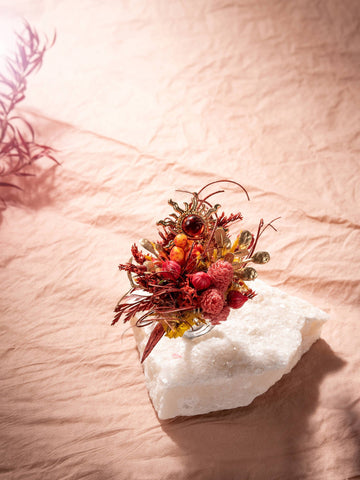 A small bouquet of dried red and yellow flowers on a white stone against a pink fabric evokes the charm of CAMELLIA's handcrafted Sun Flower Ring from New York. A small bouquet of dried red and yellow flowers on a white stone against a pink fabric evokes the charm of CAMELLIA's handcrafted Sun Flower Ring from New York.