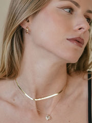 A person with long hair is wearing a 14K Yellow Gold Vermeil necklace, a star-shaped pendant, and CAMELLIA's Starburst Cz Hoops.