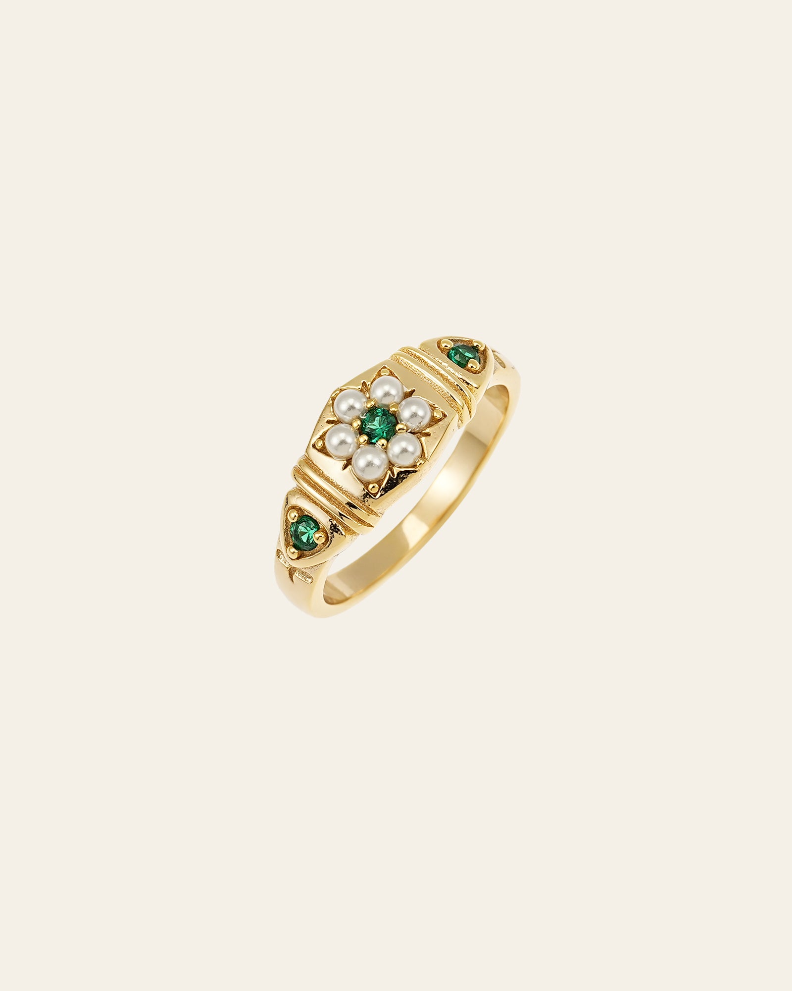 The CAMELLIA Charlotte Pearl Emerald Ring showcases a floral design of pearls and brilliant green emeralds set on a plain background.