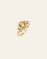 The Elara Citrine Ring by CAMELLIA is a gold piece featuring a central citrine, small clear stones, and ornate scrollwork on the band.