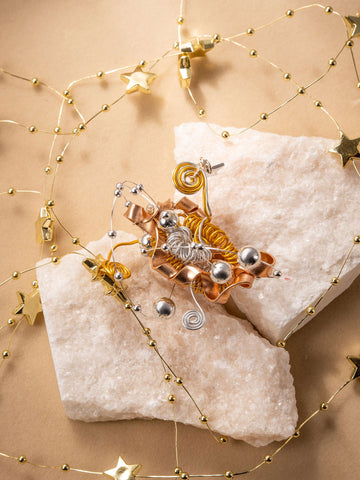CAMELLIA's Star Flower Ring, paired with festive earrings featuring metallic spirals and beads on white stones, is adorned by a gold star and bead garland on a beige background, creating an elegant handcrafted jewelry ensemble. CAMELLIA's Star Flower Ring, paired with festive earrings featuring metallic spirals and beads on white stones, is adorned by a gold star and bead garland on a beige background, creating an elegant handcrafted jewelry ensemble.