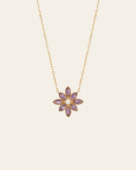 The Cámellia Amethyst Pearl Necklace by CAMELLIA features shimmering amethyst gemstones and a central yellow gem in a flower-shaped pendant crafted from 14K Yellow Gold Vermeil, set against a light background.