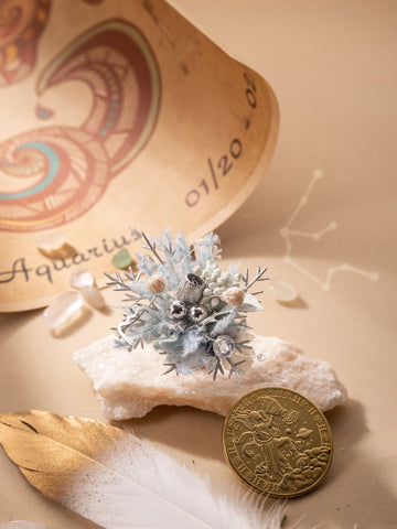 A zodiac-themed scroll, floral piece on a rock, crystals, and a golden coin beautifully surround the exquisite Aquarius Flower Ring by CAMELLIA, handcrafted in New York. A delicate feather rests gently on the beige background. A zodiac-themed scroll, floral piece on a rock, crystals, and a golden coin beautifully surround the exquisite Aquarius Flower Ring by CAMELLIA, handcrafted in New York. A delicate feather rests gently on the beige background.