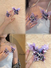 The CAMELLIA Customized Symbol Flower Ring, featuring purple and pink floral appliques on sheer fabric, is adjustable and elegantly worn on clothing against a beige wall.