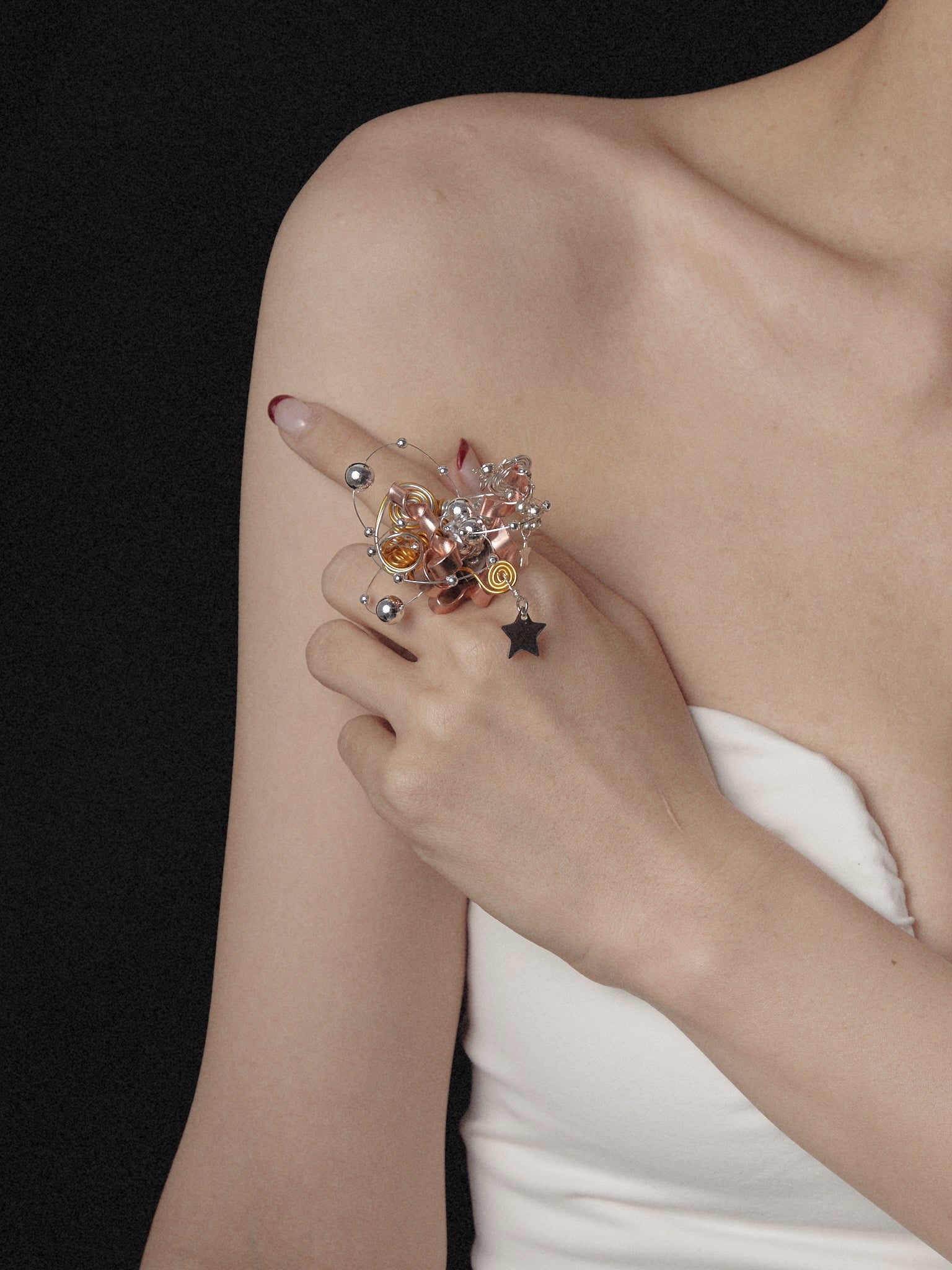 In a black backdrop, someone in a strapless white top displays the CAMELLIA Star Flower Ring, which features adjustable wire designs with intricate beads and a star charm.