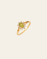 The Aurora Peridot Ring by CAMELLIA is a gold ring featuring a stunning oval Peridot gemstone, encircled by small white stones, set on a subtle background.
