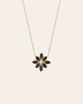 The CAMELLIA Cámellia Black Onyx Pearl Necklace features a gold chain with a floral pendant, highlighting six petal-shaped black onyx stones encircling a central pearl-like bead.