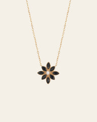 The CAMELLIA Cámellia Black Onyx Pearl Necklace features a gold chain with a floral pendant, highlighting six petal-shaped black onyx stones encircling a central pearl-like bead.
