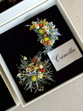 Two artistic brooches featuring multicolored flowers and foliage, labeled "CAMELLIA," exhibit the sophistication of handcrafted jewelry and are presented in a black-lined box.