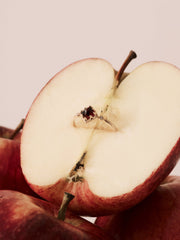 The CAMELLIA 14K Solid Gold Carena Garnet Ring, accented with small diamonds, rests on a halved red apple with more apples in the background.