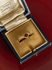 The CAMELLIA 14K Solid Gold Carena Garnet Ring is showcased in an open blue and beige jewelry box on a red surface.