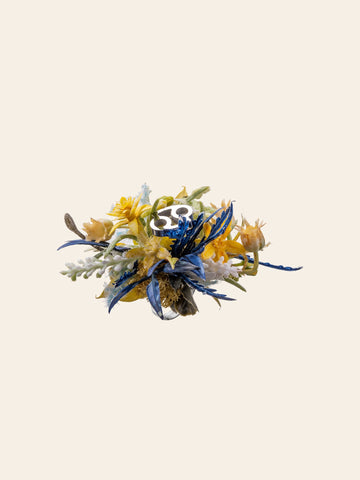 The Cancer Flower Ring by CAMELLIA features a vibrant, handcrafted floral and leaf design in blue, yellow, and green on a plain background, made in New York. The Cancer Flower Ring by CAMELLIA features a vibrant, handcrafted floral and leaf design in blue, yellow, and green on a plain background, made in New York.