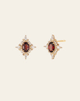 CAMELLIA's Claire Garnet Diamond Earrings showcase a central red gemstone accented by small white stones in a starburst design, all set in gold against a plain light background.