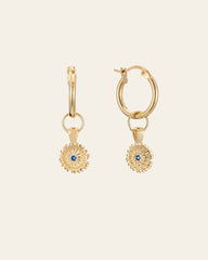 The Elsa Peony Sapphire Earrings by CAMELLIA are gold hoops with sunflower-shaped pendants, featuring a central blue sapphire. Handcrafted in New York and set in 14K yellow gold vermeil, these earrings beautifully showcase artisanal craftsmanship against a plain background.