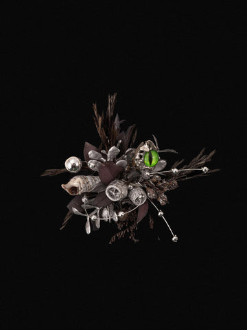 The Devil's Eye Flower Ring by CAMELLIA, featuring a detailed design of dried leaves, twigs, silver ornaments, a shell, and a bright green bead against a black background, captures the essence of handcrafted artistry in New York. The Devil's Eye Flower Ring by CAMELLIA, featuring a detailed design of dried leaves, twigs, silver ornaments, a shell, and a bright green bead against a black background, captures the essence of handcrafted artistry in New York.
